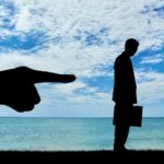 Silhouette di professionista con valigetta respinto da una mano, simbolo di straining lavorativo e mobbing