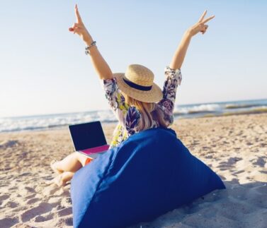 Donna lavora da remoto con laptop in spiaggia tropicale, smart working e telelavoro