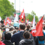 Manifestazione sindacale con bandiere rosse e svizzere, protesta diritti lavoratori e contratti collettivi
