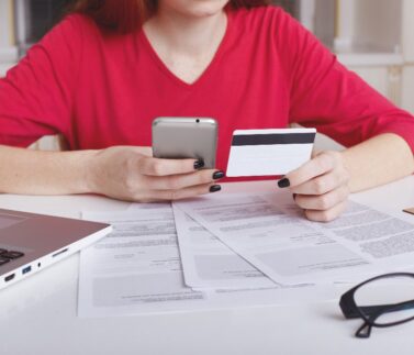 il-modello-femminile-irriconoscibile-in-maglione-rosso-si-siede-al-tavolo-di-lavoro-circondato-da-documenti-e-computer-portatile