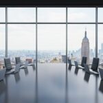 Sala riunioni panoramica con tavolo e sedie nere, vista sulla città e grattacieli, contesto aziendale professionale