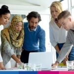 Gruppo multietnico di professionisti riuniti attorno a un laptop in riunione di lavoro collaborativa