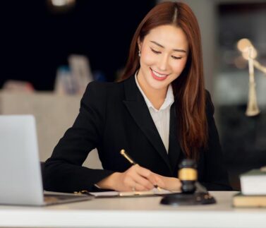 Avvocato donna che scrive documenti legali in studio con statuetta della Giustizia