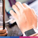 Clessidra con sabbia e mano d'uomo con smartwatch su scrivania, simbolo di gestione del tempo in ambito legale e fiscale