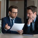 Due professionisti in abito da lavoro analizzano documento durante riunione d'affari in ufficio