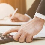 Professionista calcola costi costruzione con calcolatrice e documenti fiscali in ufficio