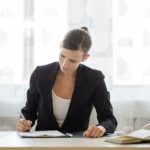 Donna professionista in abito da lavoro scrive su documenti alla scrivania in ufficio moderno
