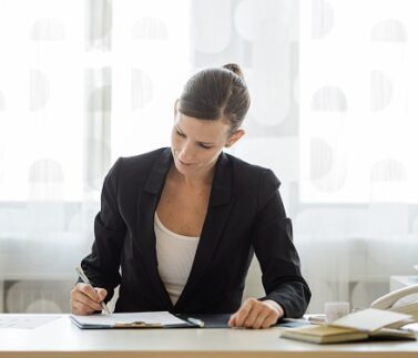 Donna professionista in abito da lavoro scrive su documenti alla scrivania in ufficio moderno