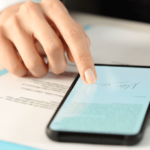 Mano tocca smartphone con documento fiscale su scrivania con fogli blu