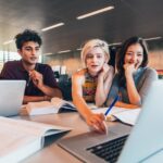 Gruppo di giovani professionisti in riunione di lavoro attorno a laptop e documenti in ufficio moderno