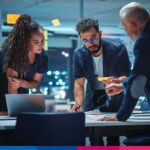 Tre professionisti discutono di strategia legale e fiscale davanti a laptop in ufficio moderno