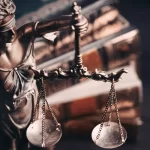 Statua della Giustizia con bilancia e libro di diritto in sfondo