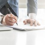 Professionista firma documento legale con penna su scrivania bianca, rappresenta consenso e accordo contrattuale