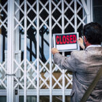 Persona appende cartello chiuso su serranda metallo - trasferimento azienda crisi d'impresa