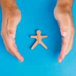 Mani che proteggono figura in legno su sfondo blu, simbolo di tutela del lavoratore e protezione legale nel lavoro